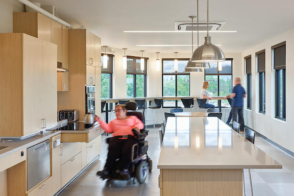 Fully accessible demonstration kitchen with wheelchair user accessing an item from a pull-out stove top.