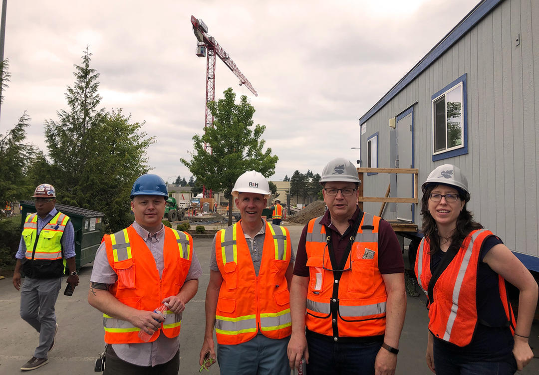 Architects, engineers, and designers celebrate the ground breaking with a large tower crane behind in the construction site